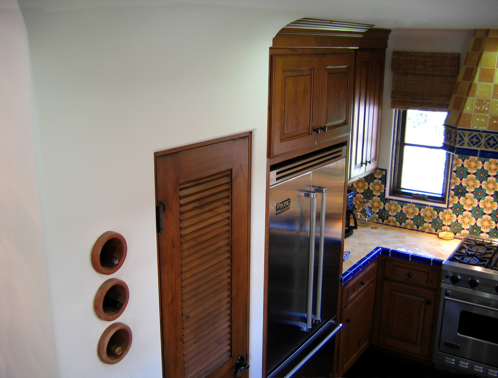 Photo of a small mediterranean u-shaped eat-in kitchen in Santa Barbara with a double-bowl sink, raised-panel cabinets, medium wood cabinets, tile benchtops, ceramic splashback, stainless steel appliances, dark hardwood floors, a peninsula, multi-coloured splashback, brown floor and yellow benchtop.