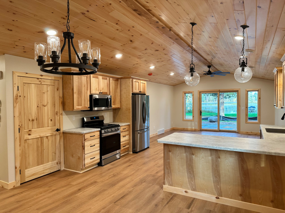 This is an example of a mid-sized country galley eat-in kitchen in Minneapolis with an undermount sink, shaker cabinets, light wood cabinets, laminate benchtops, stainless steel appliances, light hardwood floors, a peninsula, white benchtop and vaulted.
