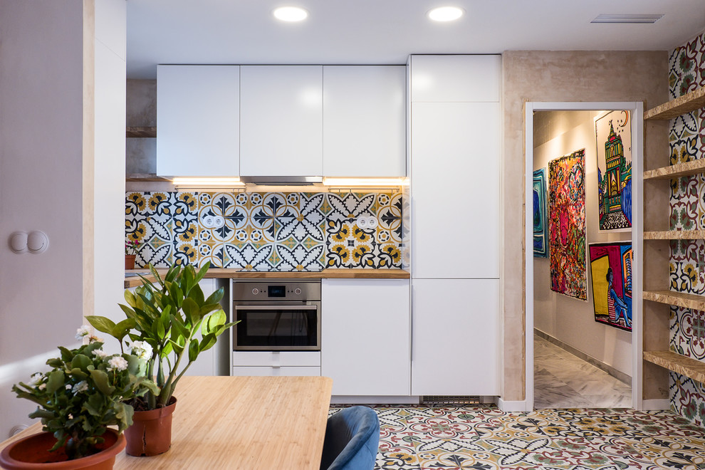 Design ideas for a small contemporary l-shaped eat-in kitchen in Seville with flat-panel cabinets, white cabinets, wood benchtops, stainless steel appliances, no island, a drop-in sink, multi-coloured splashback, multi-coloured floor and beige benchtop.