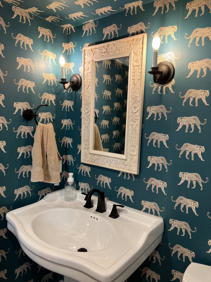 This is an example of a small traditional powder room in Boston with a one-piece toilet, blue walls, wood-look tile, a pedestal sink, brown floor, a freestanding vanity, wallpaper and wallpaper.