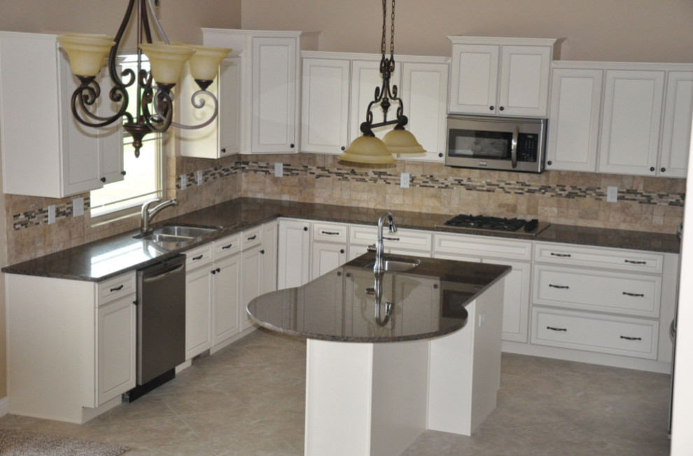 Mid-sized elegant l-shaped travertine floor and beige floor enclosed kitchen photo with a double-bowl sink, recessed-panel cabinets, white cabinets, granite countertops, beige backsplash, stone tile backsplash, stainless steel appliances and an island