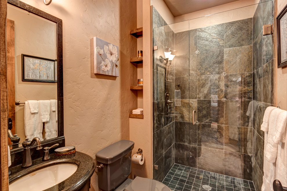 Alcove shower - mid-sized rustic black tile, brown tile and slate tile multicolored floor alcove shower idea with a two-piece toilet, beige walls, an undermount sink, granite countertops, a hinged shower door and black countertops