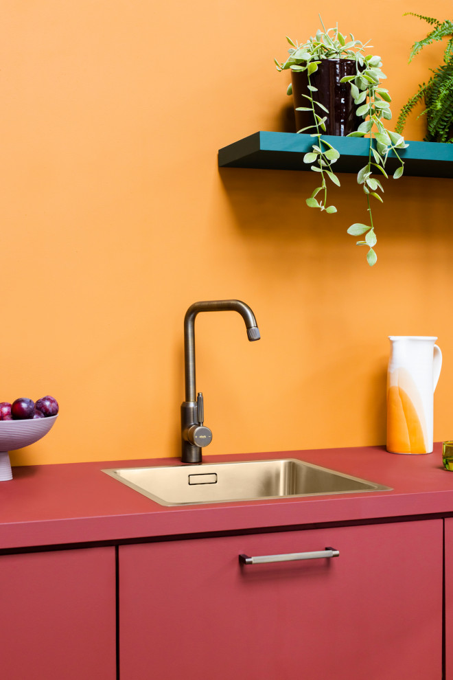 Small modern single-wall open plan kitchen in London with a single-bowl sink, flat-panel cabinets, red cabinets, wood worktops, orange splashback, wood splashback and red worktops.