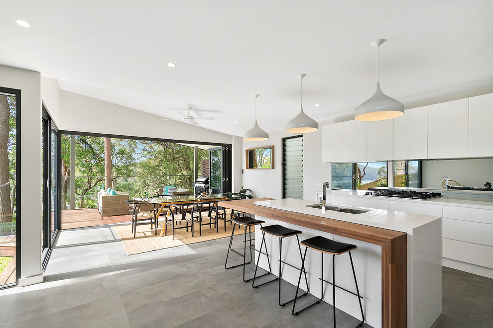 Large modern galley kitchen in Sunshine Coast with a double-bowl sink, recessed-panel cabinets, white cabinets, wood benchtops, grey splashback, mirror splashback, stainless steel appliances, light hardwood floors, with island, grey floor and white benchtop.