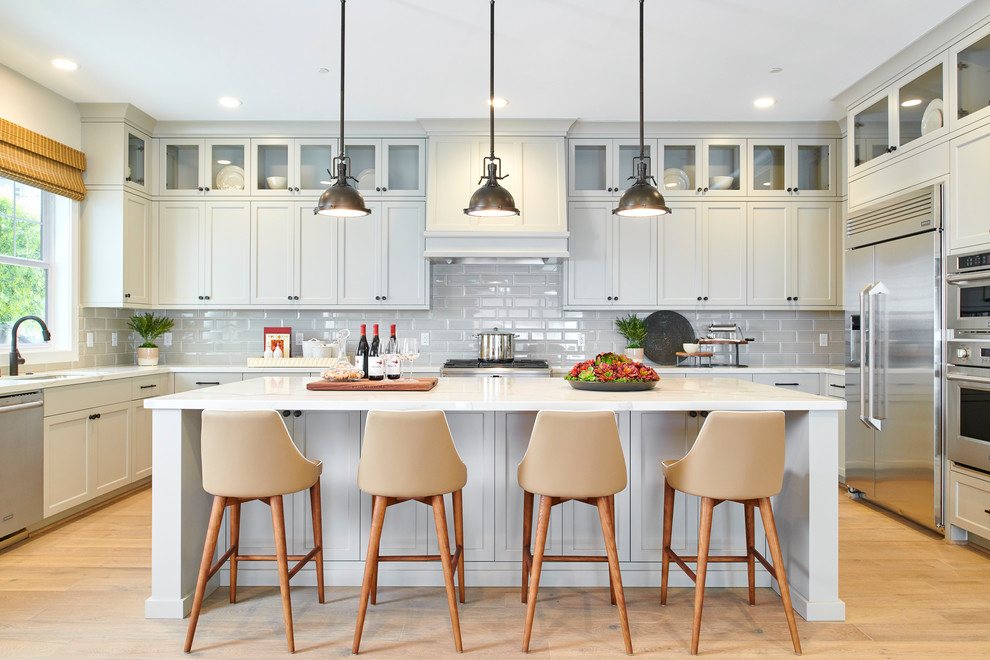Example of a transitional u-shaped light wood floor enclosed kitchen design in San Francisco with an undermount sink, shaker cabinets, gray cabinets, beige backsplash, subway tile backsplash, stainless steel appliances, an island and white countertops