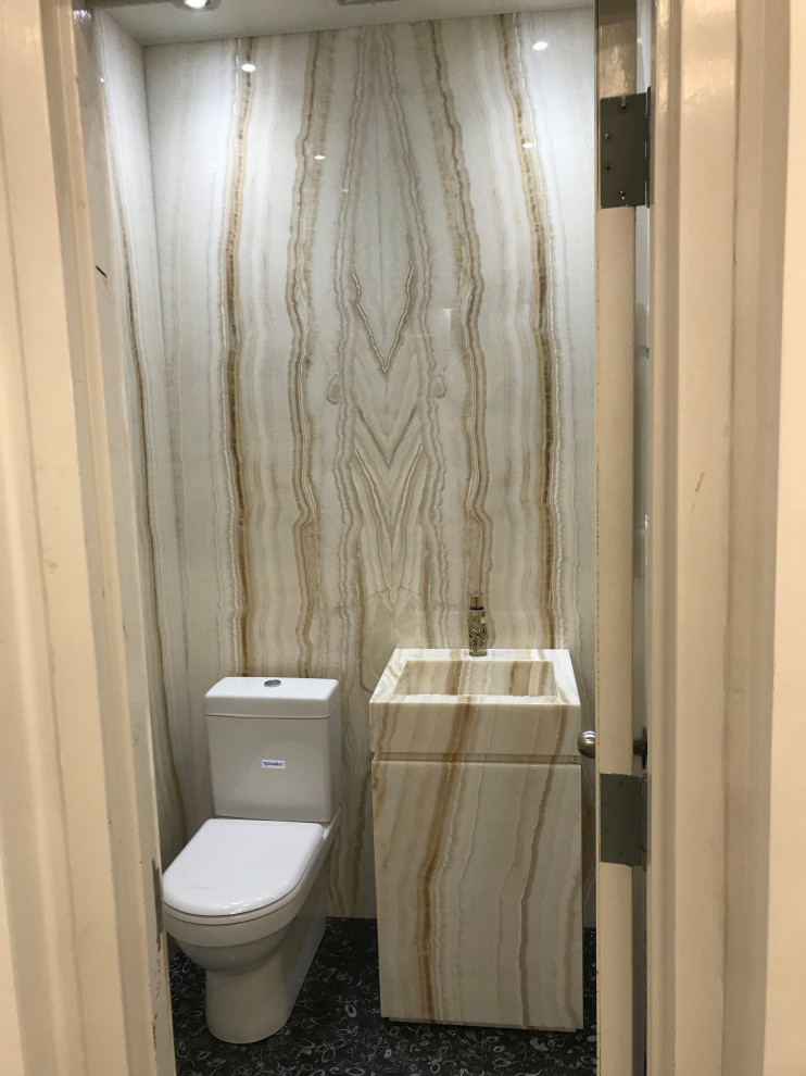 Bild på ett litet funkis beige beige toalett, med släta luckor, beige skåp, en toalettstol med hel cisternkåpa, beige kakel, marmorkakel, beige väggar, skiffergolv, ett integrerad handfat, marmorbänkskiva och svart golv