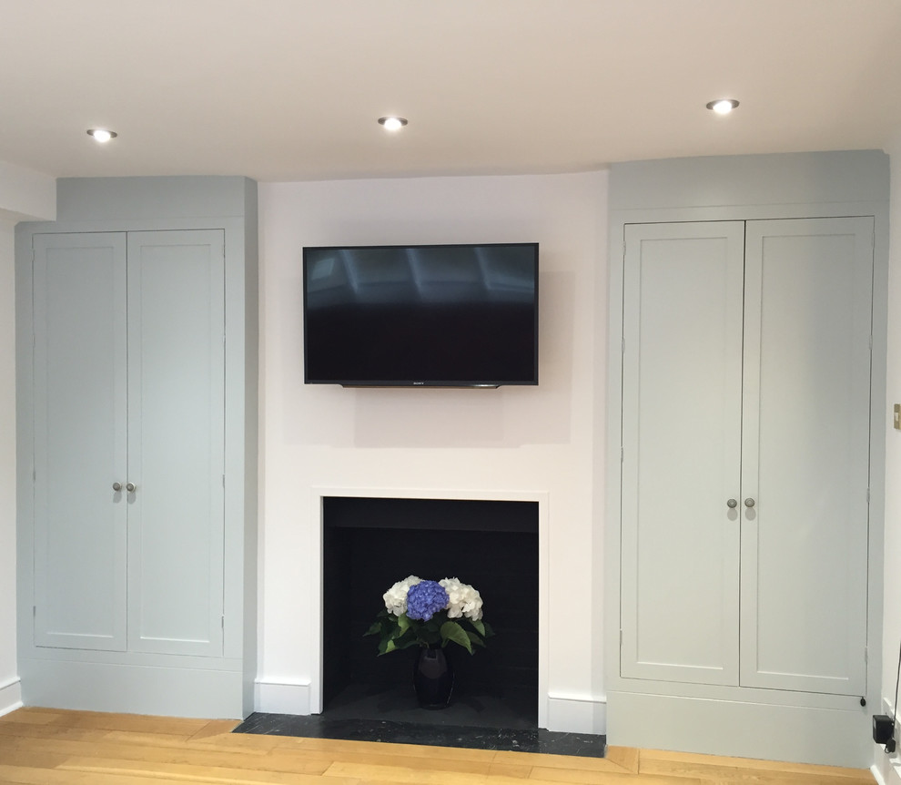 Mid-sized contemporary enclosed family room in London with white walls, medium hardwood floors, a standard fireplace, a plaster fireplace surround and a wall-mounted tv.
