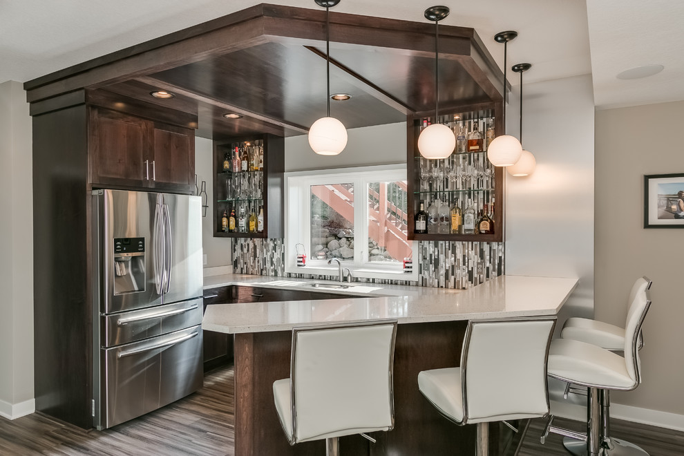 Photo of a transitional u-shaped seated home bar in Minneapolis with an undermount sink, shaker cabinets, dark wood cabinets, multi-coloured splashback, matchstick tile splashback, brown floor and white benchtop.