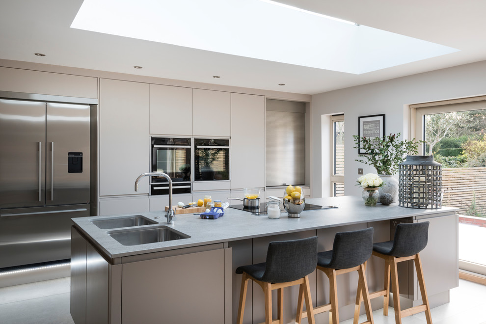 This is an example of a large contemporary open plan kitchen in West Midlands with a double-bowl sink, quartzite benchtops, stainless steel appliances, grey benchtop, flat-panel cabinets, grey cabinets and with island.
