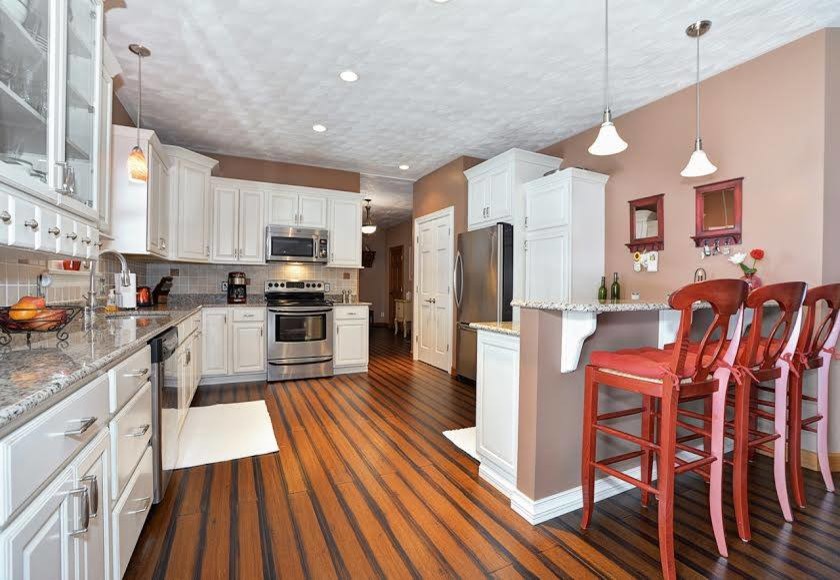 Inspiration for a transitional bamboo floor eat-in kitchen remodel with raised-panel cabinets, white cabinets, granite countertops, beige backsplash, ceramic backsplash and stainless steel appliances