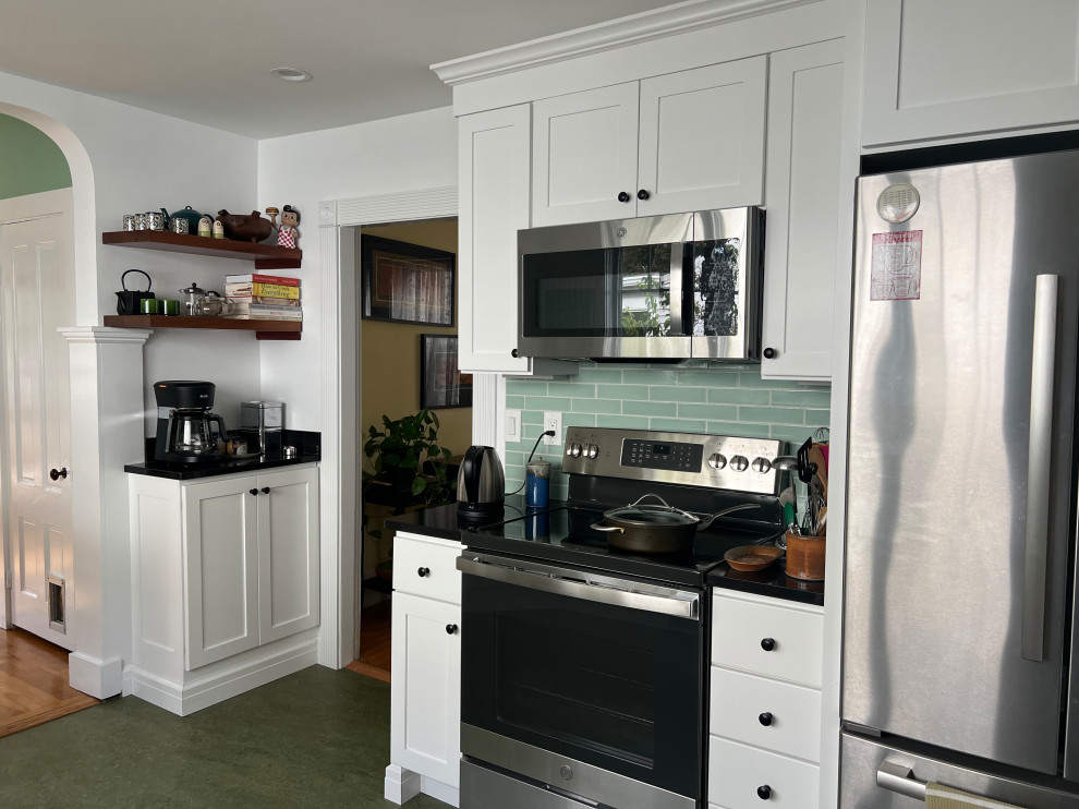 Photo of a mid-sized transitional l-shaped eat-in kitchen in Boston with a farmhouse sink, shaker cabinets, white cabinets, quartz benchtops, green splashback, ceramic splashback, stainless steel appliances, linoleum floors, a peninsula, green floor and black benchtop.