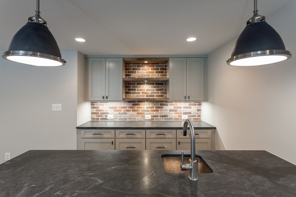 Inspiration for a traditional galley wet bar in DC Metro with brown floor, an undermount sink, shaker cabinets, grey cabinets, multi-coloured splashback, brick splashback and black benchtop.