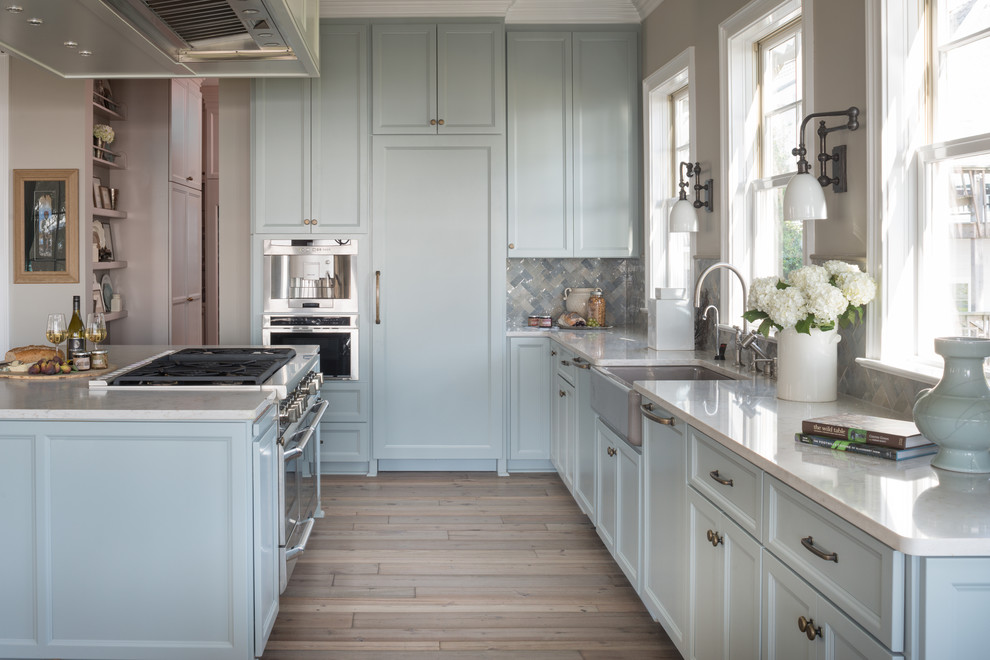 Inspiration for a beach style l-shaped kitchen in Other with quartz benchtops, with island, a farmhouse sink, recessed-panel cabinets, blue cabinets, multi-coloured splashback, panelled appliances and medium hardwood floors.