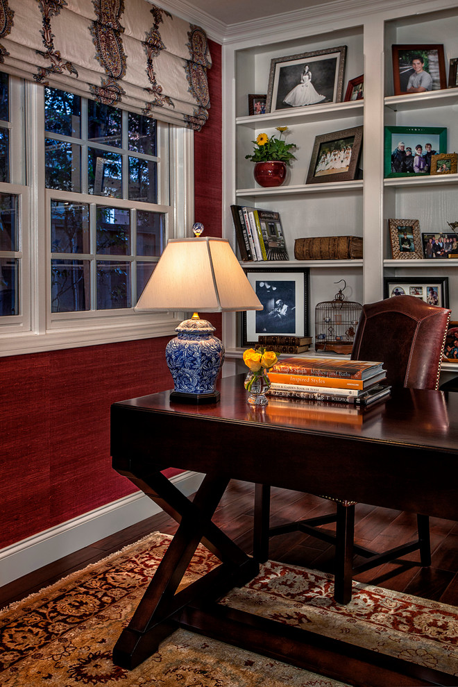 This is an example of a traditional study room in Orange County with red walls, dark hardwood floors and a freestanding desk.
