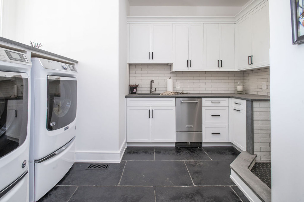Photo of a modern utility room in Baltimore with an undermount sink, shaker cabinets, white cabinets, beige splashback, matchstick tile splashback, white walls, a side-by-side washer and dryer, black floor and grey benchtop.