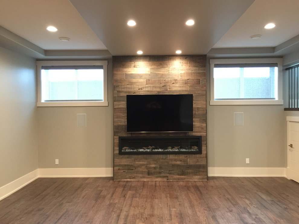 Mid-sized mountain style underground medium tone wood floor and brown floor basement photo in Edmonton with gray walls, a standard fireplace and a wood fireplace surround