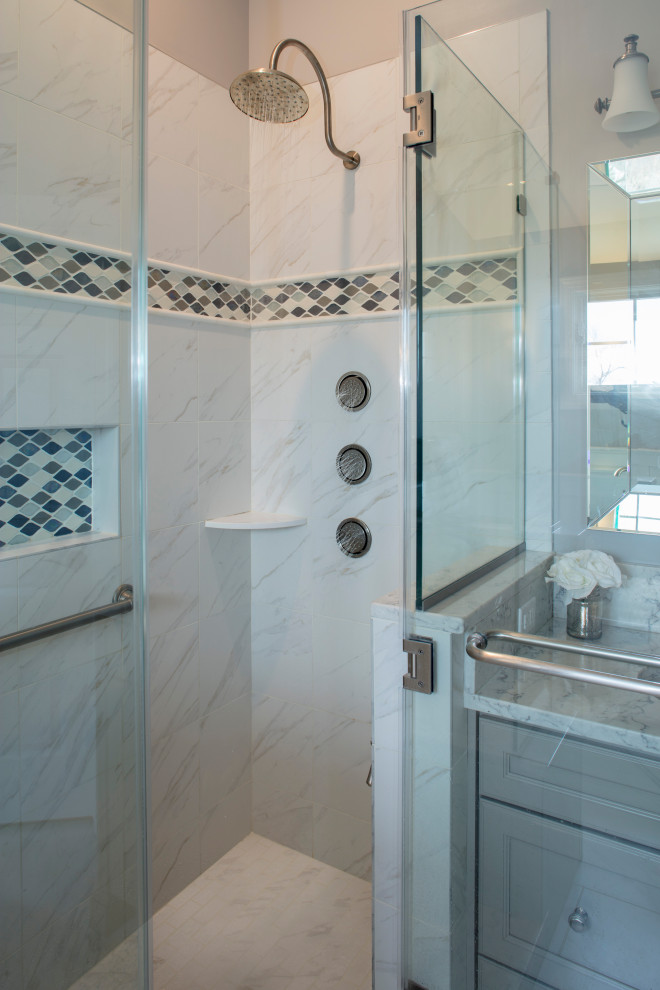 Photo of a large contemporary master bathroom in Philadelphia with recessed-panel cabinets, grey cabinets, a freestanding tub, a double shower, a two-piece toilet, gray tile, ceramic tile, grey walls, ceramic floors, an undermount sink, marble benchtops, grey floor, a hinged shower door, grey benchtops, a shower seat, a double vanity, a built-in vanity and decorative wall panelling.