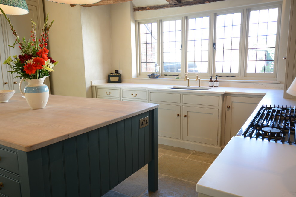 Large country u-shaped open plan kitchen in Sussex with beaded inset cabinets, beige cabinets, quartzite benchtops, white splashback, panelled appliances, limestone floors, with island, white benchtop, an integrated sink and green floor.