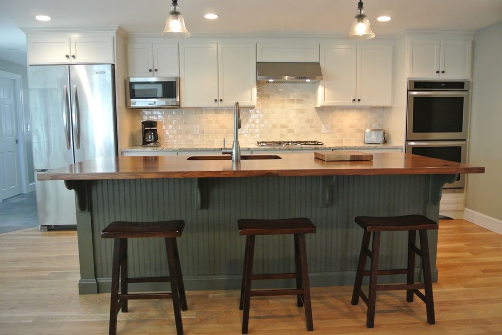 Eat-in kitchen - transitional galley light wood floor eat-in kitchen idea in Boston with an undermount sink, stainless steel appliances, an island, shaker cabinets, white cabinets, wood countertops, white backsplash, ceramic backsplash and brown countertops