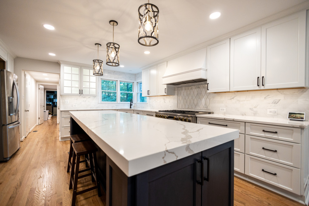Example of a large transitional l-shaped light wood floor and brown floor eat-in kitchen design in Baltimore with an undermount sink, shaker cabinets, white cabinets, quartz countertops, white backsplash, marble backsplash, stainless steel appliances, an island and white countertops