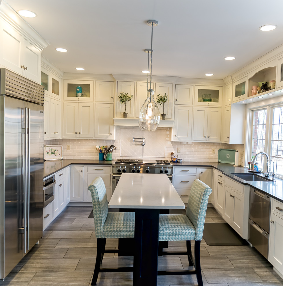 Large transitional u-shaped medium tone wood floor and brown floor eat-in kitchen photo with an undermount sink, shaker cabinets, white cabinets, solid surface countertops, white backsplash, subway tile backsplash, stainless steel appliances and an island
