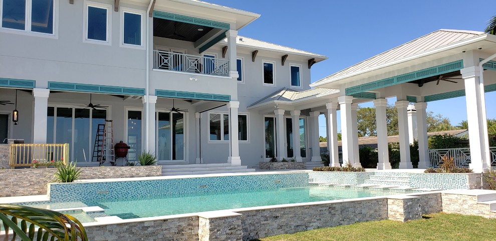 Photo of an expansive beach style two-storey stucco grey house exterior in Tampa with a hip roof and a metal roof.