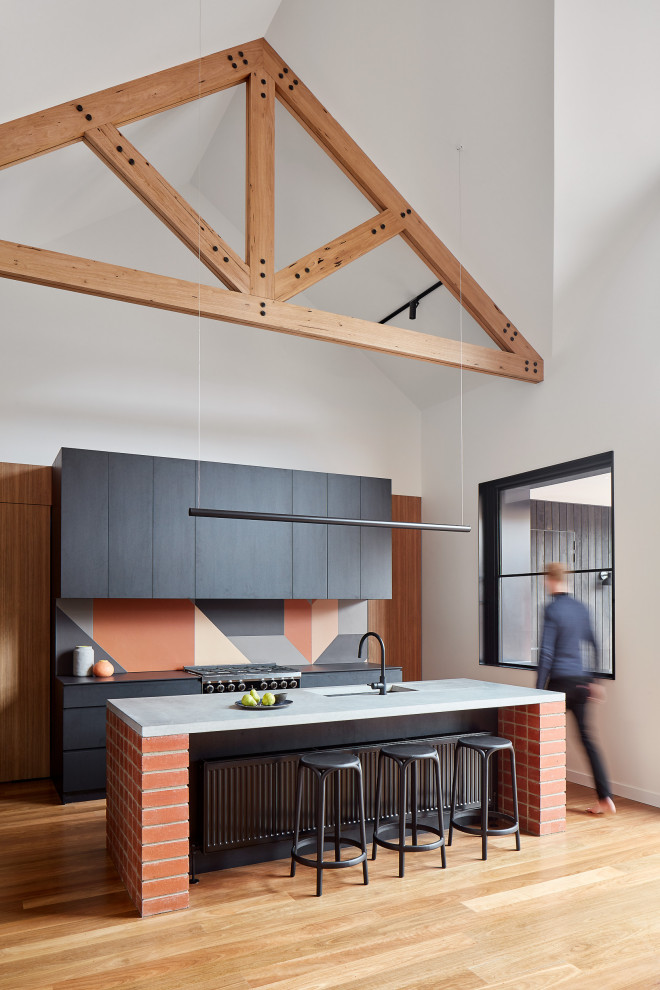 Inspiration for a contemporary kitchen in Melbourne with an integrated sink, flat-panel cabinets, black cabinets, concrete benchtops, terra-cotta splashback, black appliances, medium hardwood floors, with island and black benchtop.