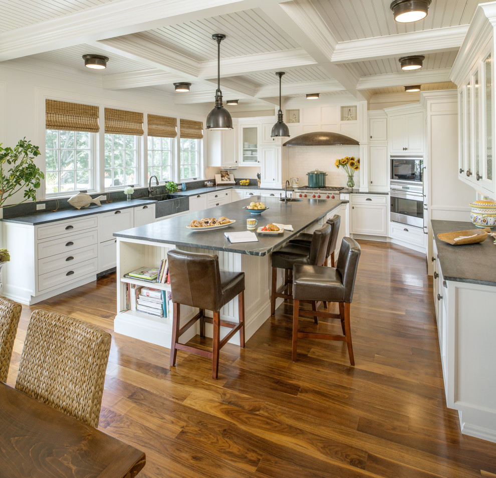 Inspiration for a beach style u-shaped open plan kitchen in Providence with a farmhouse sink, shaker cabinets, white cabinets, stainless steel appliances, dark hardwood floors and with island.