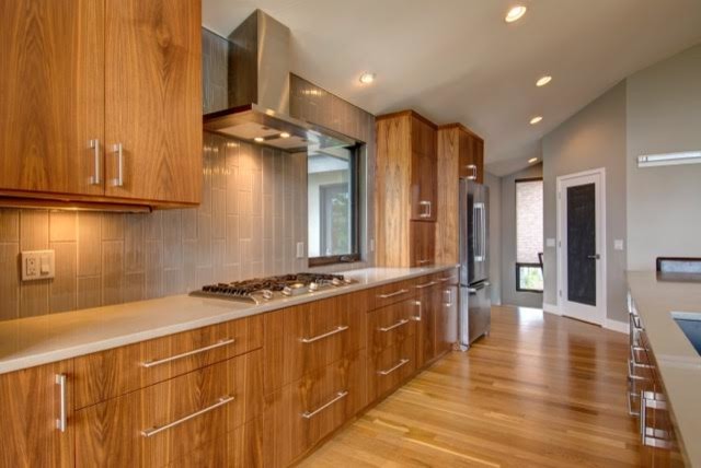Design ideas for a large midcentury galley kitchen pantry in Denver with an undermount sink, flat-panel cabinets, medium wood cabinets, granite benchtops, beige splashback, ceramic splashback, stainless steel appliances, light hardwood floors and with island.