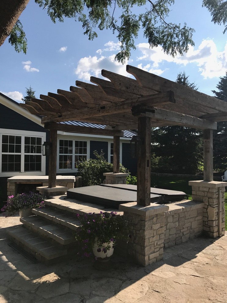 Inspiration for a country backyard patio in Milwaukee with natural stone pavers and a pergola.