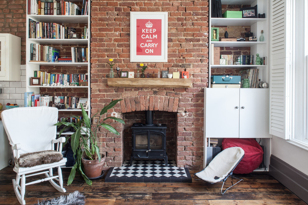 Photo of a country living room in London with a library, dark hardwood floors, a wood stove and a brick fireplace surround.