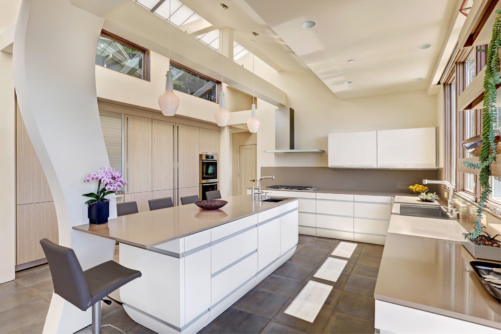 This is an example of a large contemporary u-shaped eat-in kitchen in San Francisco with a single-bowl sink, flat-panel cabinets, quartz benchtops, grey splashback, stainless steel appliances, with island, white cabinets and slate floors.