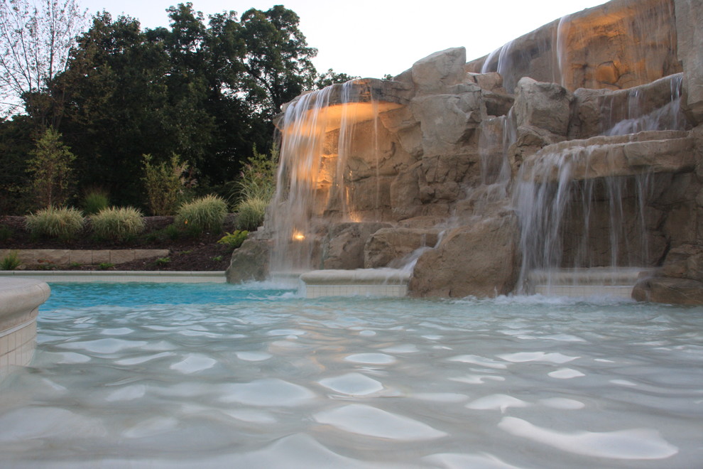 This is an example of a mid-sized beach style backyard custom-shaped natural pool in Chicago with a water feature and stamped concrete.
