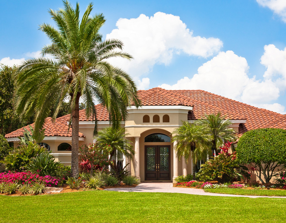 This is an example of a large tropical one-storey stucco beige exterior in Orange County with a hip roof.