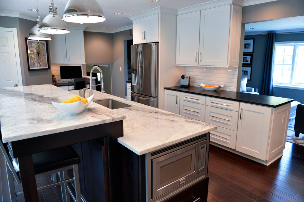 Inspiration for a transitional dark wood floor kitchen remodel in Cleveland with a drop-in sink, recessed-panel cabinets, white backsplash, ceramic backsplash, stainless steel appliances and an island