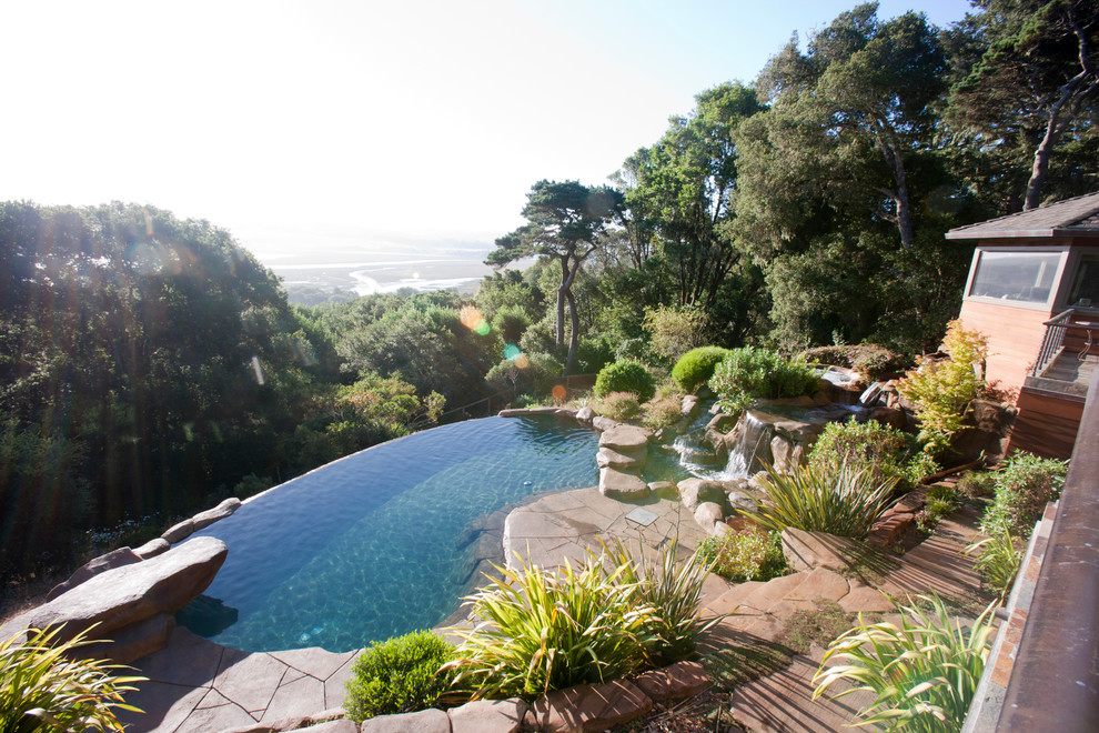This is an example of a large tropical backyard custom-shaped infinity pool in San Francisco with a hot tub and natural stone pavers.