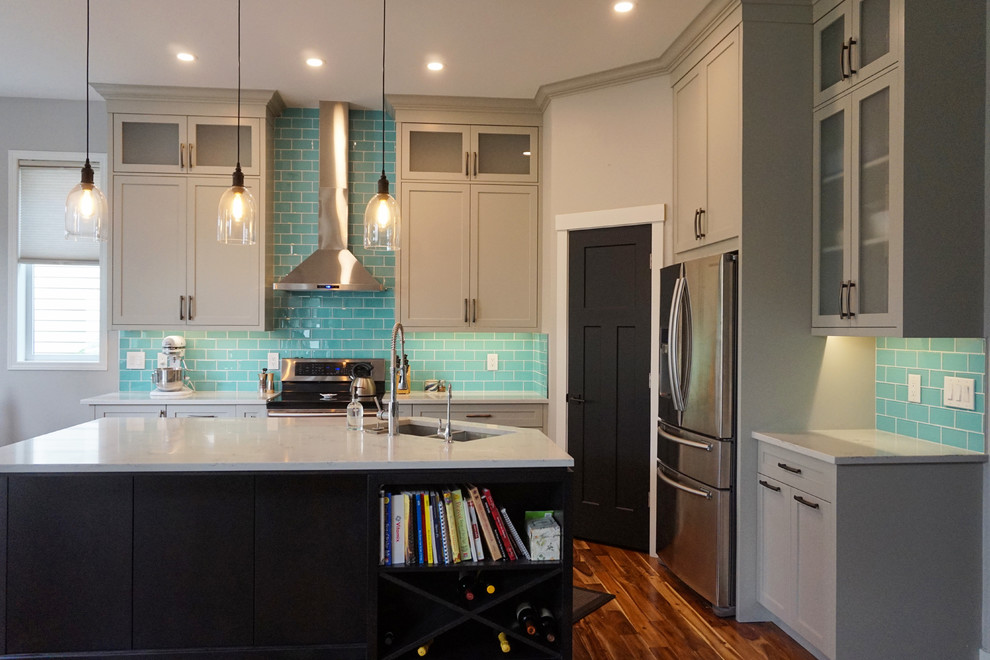 Example of a mid-sized transitional l-shaped medium tone wood floor and brown floor kitchen design in Calgary with an undermount sink, shaker cabinets, gray cabinets, quartz countertops, blue backsplash, ceramic backsplash, stainless steel appliances and an island