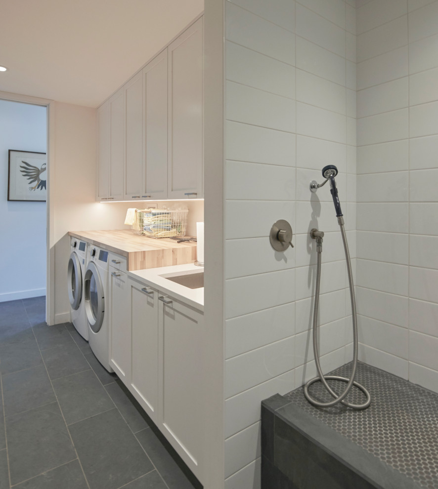 This is an example of a large country single-wall dedicated laundry room in Chicago with an undermount sink, shaker cabinets, white cabinets, wood benchtops, white walls, slate floors, a side-by-side washer and dryer, grey floor and brown benchtop.