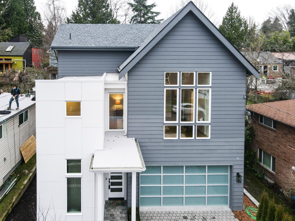 Пример оригинального дизайна: двухэтажный, синий частный загородный дом среднего размера в стиле модернизм с облицовкой из винила, двускатной крышей, черепичной крышей, серой крышей и отделкой доской с нащельником