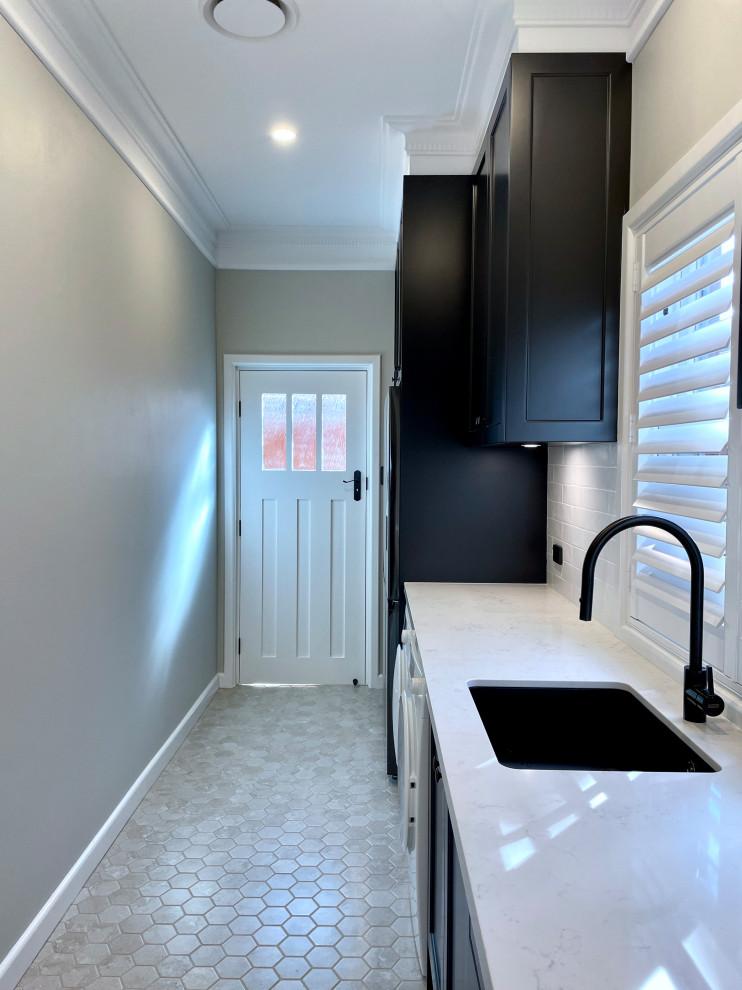 Large traditional single-wall separated utility room in Sydney with a submerged sink, recessed-panel cabinets, black cabinets, engineered stone countertops, white splashback, metro tiled splashback, grey walls, marble flooring, a side by side washer and dryer, grey floors and white worktops.