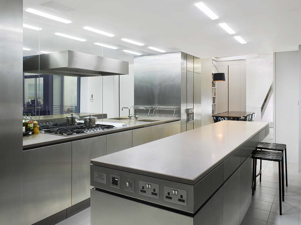 Large contemporary galley open plan kitchen in London with a drop-in sink, stainless steel cabinets, metallic splashback, mirror splashback, stainless steel appliances and with island.