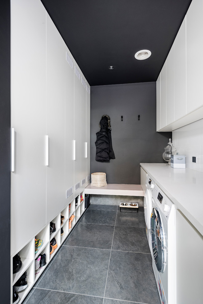 Photo of a large modern galley laundry room in Melbourne with flat-panel cabinets, white cabinets, quartz benchtops, porcelain floors, a side-by-side washer and dryer, grey floor, white benchtop and grey walls.