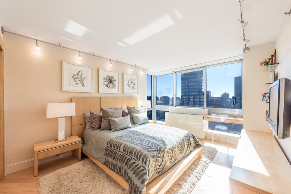 This is an example of a large contemporary master bedroom in New York with beige walls, light hardwood floors and no fireplace.