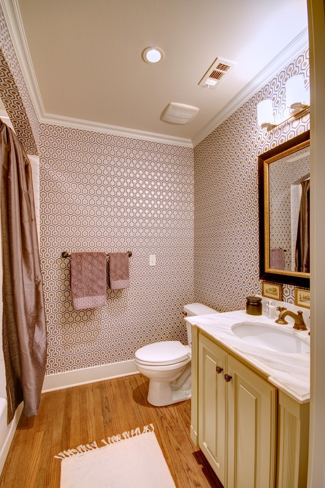 This is an example of a large traditional powder room in Austin with an undermount sink, raised-panel cabinets, marble benchtops, a two-piece toilet, white tile, medium hardwood floors and yellow cabinets.