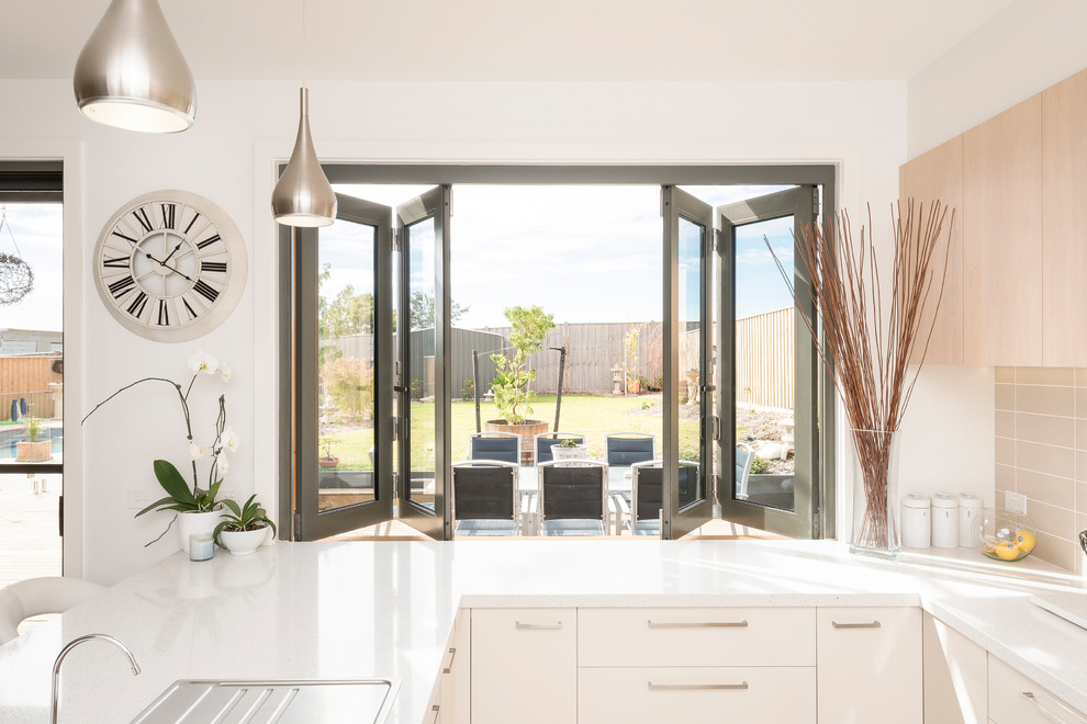 Design ideas for a mid-sized beach style u-shaped open plan kitchen in Geelong with a double-bowl sink, light wood cabinets, quartz benchtops, beige splashback, ceramic splashback, stainless steel appliances and porcelain floors.