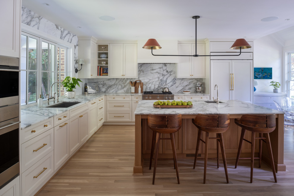 Example of a transitional l-shaped light wood floor and beige floor kitchen design in DC Metro with an undermount sink, recessed-panel cabinets, beige cabinets, gray backsplash, stone slab backsplash, paneled appliances, an island and gray countertops