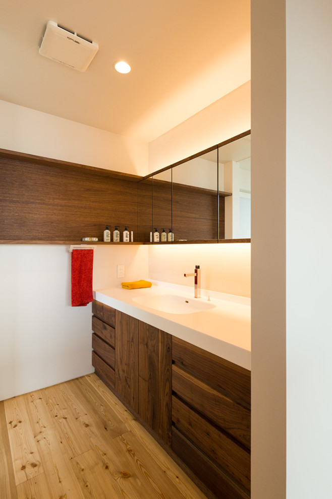 他の地域にあるアジアンスタイルのおしゃれなトイレ・洗面所 (フラットパネル扉のキャビネット、中間色木目調キャビネット、白い壁、無垢フローリング、一体型シンク、茶色い床) の写真