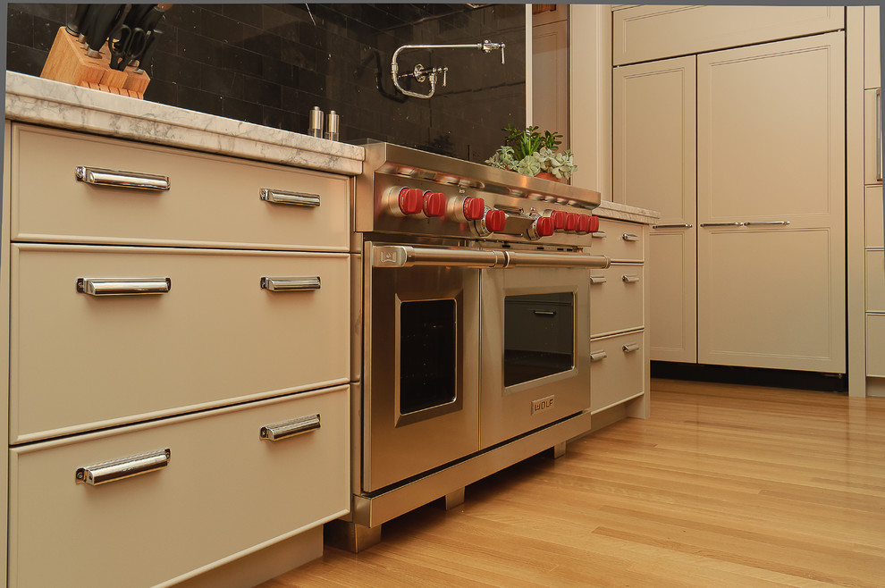 Eat-in kitchen - large transitional l-shaped light wood floor eat-in kitchen idea in Calgary with beige cabinets, granite countertops, black backsplash, subway tile backsplash, paneled appliances, an island and a farmhouse sink