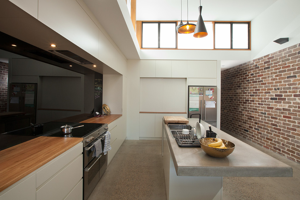 Photo of a mid-sized contemporary galley open plan kitchen in Sydney with an integrated sink, white cabinets, concrete benchtops, black splashback, glass sheet splashback, concrete floors, with island and stainless steel appliances.
