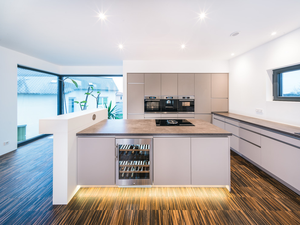 Inspiration for a mid-sized modern l-shaped kitchen in Frankfurt with flat-panel cabinets, beige cabinets, black appliances, bamboo floors, with island, brown floor and brown benchtop.